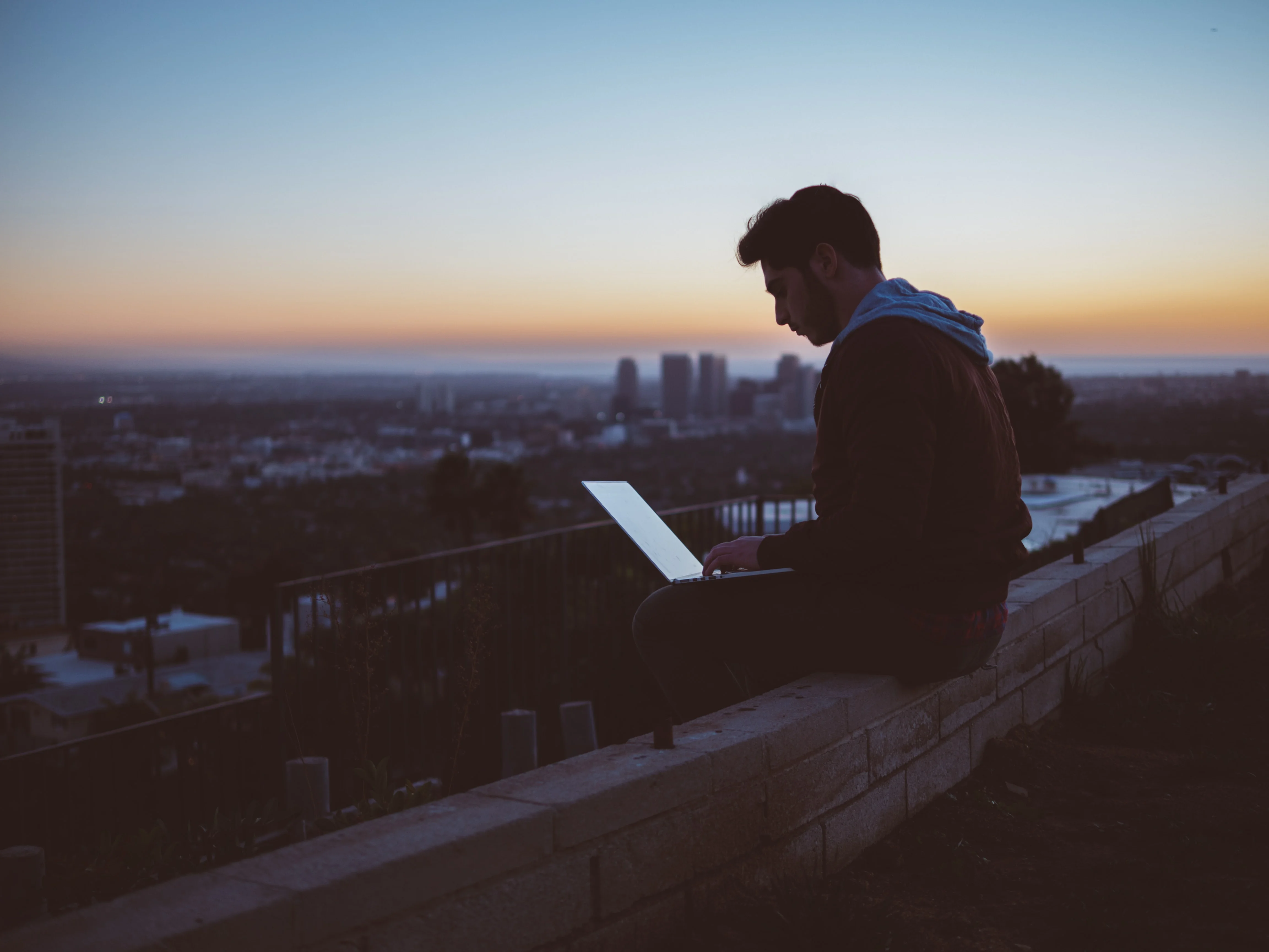 Un uomo seduto su una sporgenza con un computer portatile
